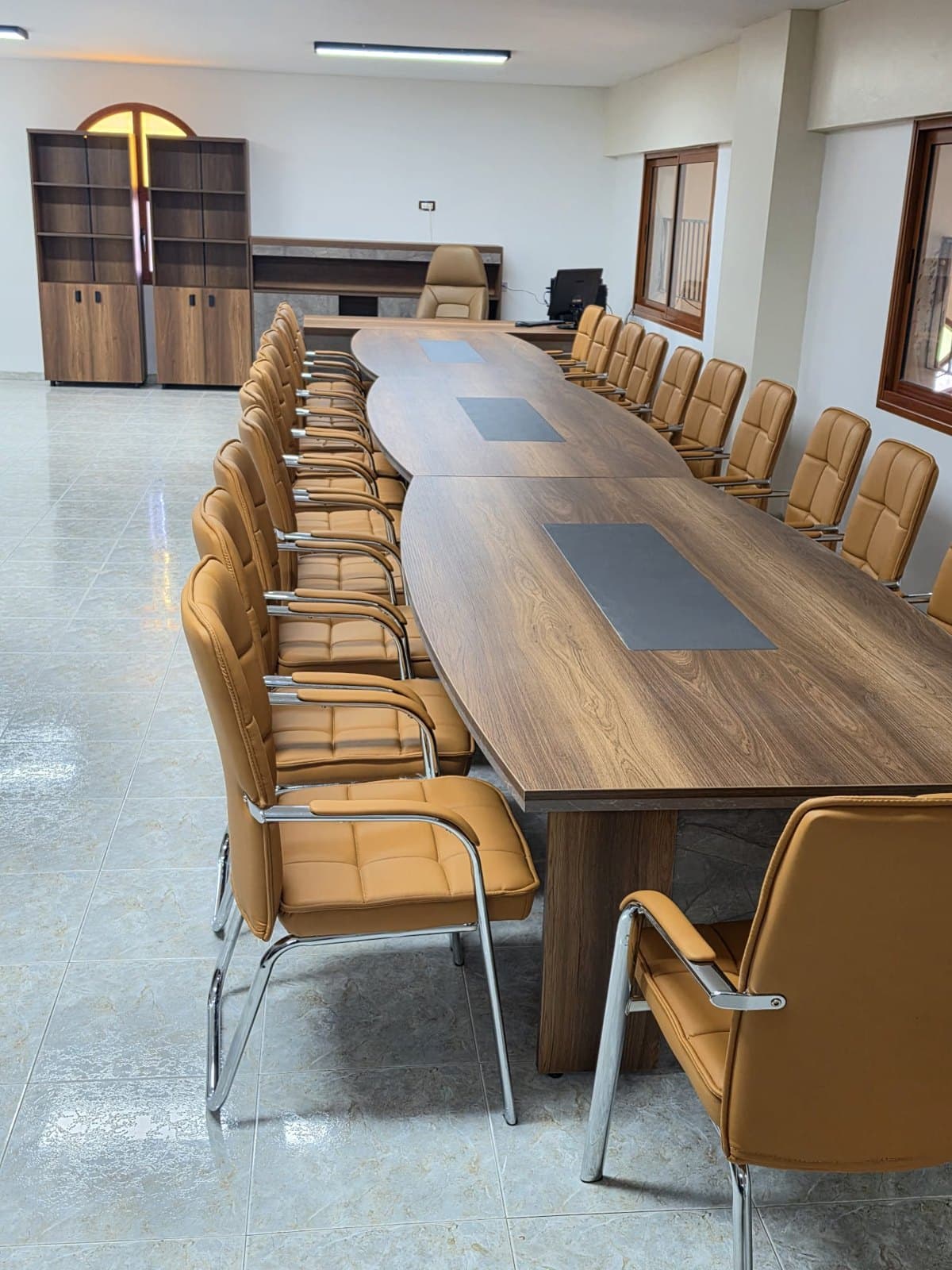 חדר ישיבות עם שולחן ארוך בגוון אגוז, משטחי כתיבה כהים וכיסאות אורח בגוון קאמל